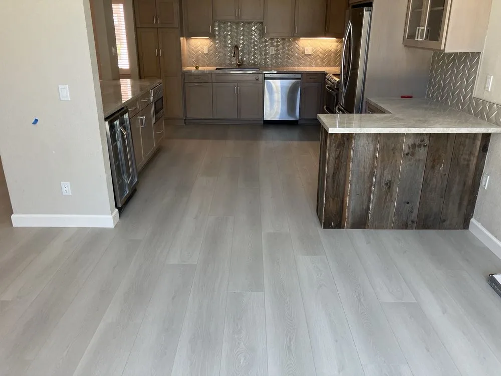 Light gray wide-plank flooring in a modern kitchen by The Flooring Design Center